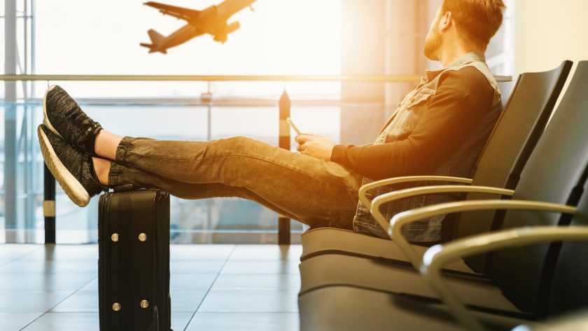 man sitting on gang chair with feet on luggage looking at airplane